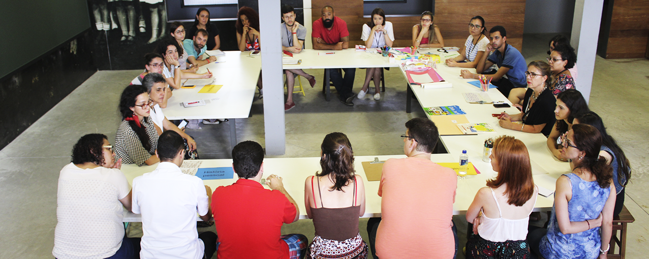 Em torno de uma mesa quadrada branca, homens e mulheres estão sentados conversando